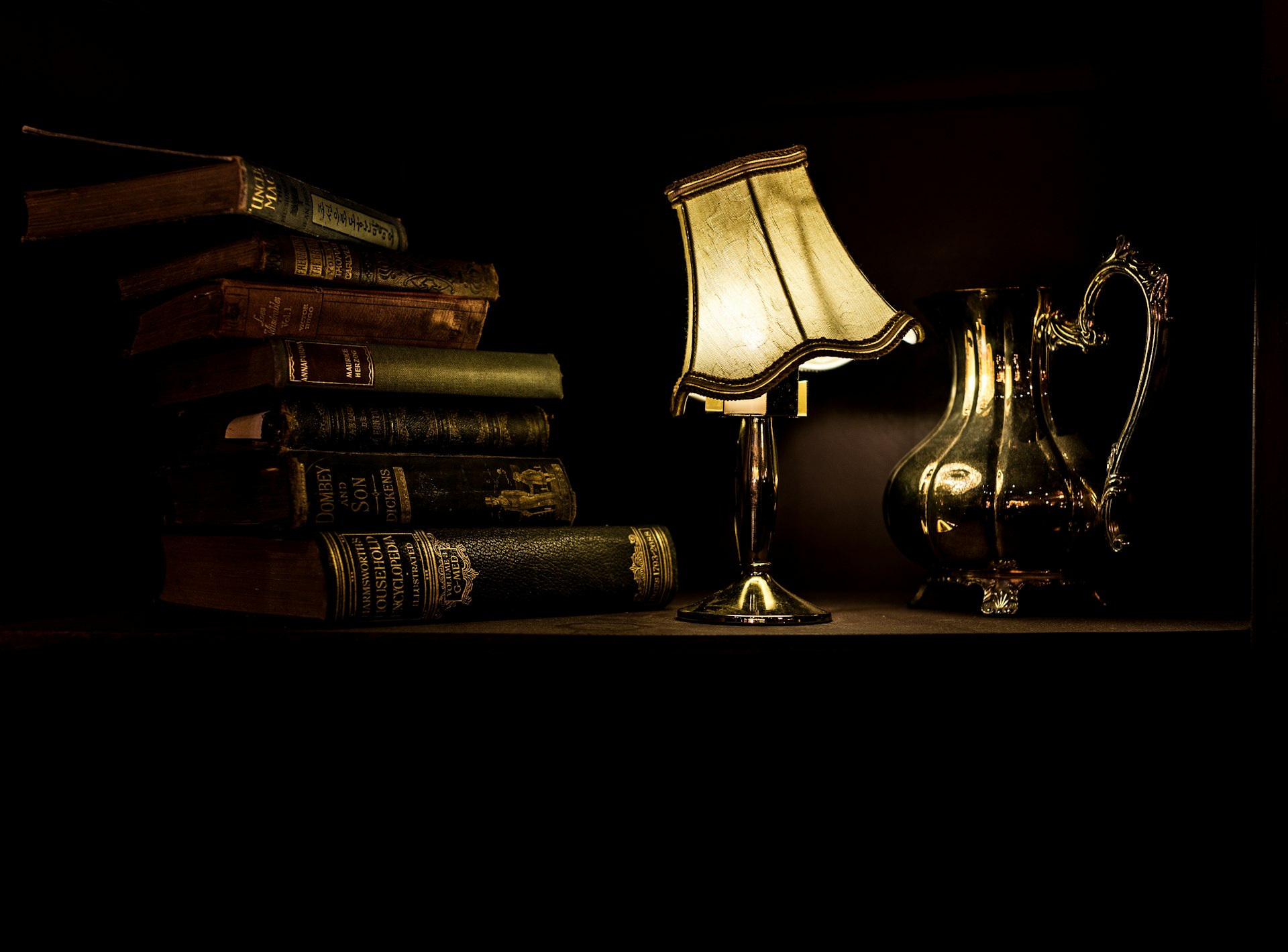 Ein Stapel Bücher neben einer brennenden Schreibtischlampe
